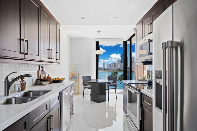 kitchen featuring sink, light tile floors, appliances with stainless steel finishes, decorative light fixtures, and dark brown cabinetry