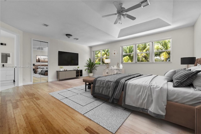 bedroom with a tray ceiling, ceiling fan, and light wood-type flooring