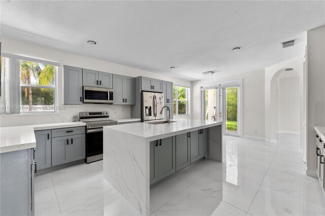 kitchen featuring light tile floors, appliances with stainless steel finishes, plenty of natural light, and an island with sink