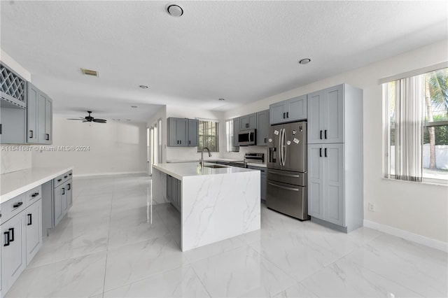 kitchen with a kitchen island with sink, ceiling fan, light tile floors, and stainless steel appliances