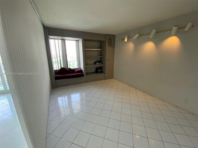 spare room featuring built in features, light tile floors, and a textured ceiling