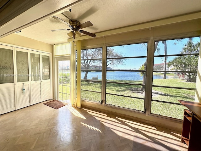 unfurnished sunroom featuring a wealth of natural light, ceiling fan, and a water view