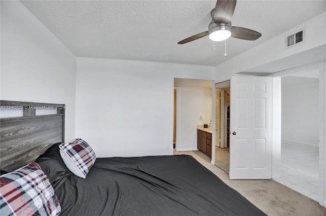 carpeted bedroom with a textured ceiling, ensuite bathroom, and ceiling fan