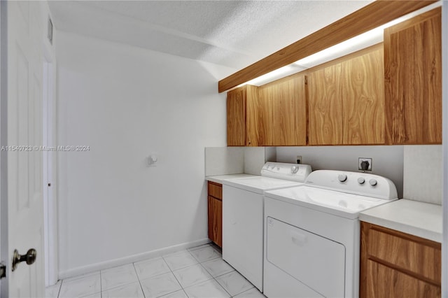 laundry room featuring washer and clothes dryer, a textured ceiling, cabinets, and light tile patterned floors