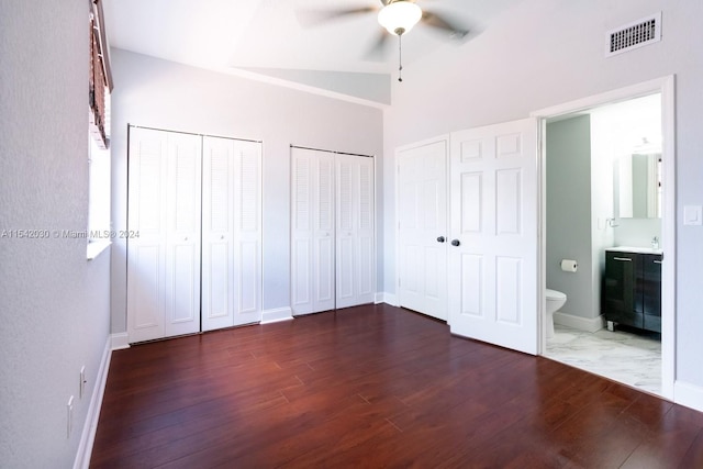 unfurnished bedroom with ensuite bath, ceiling fan, dark hardwood / wood-style flooring, lofted ceiling, and two closets