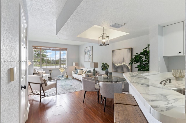 dining room with a raised ceiling, dark hardwood / wood-style flooring, a textured ceiling, and sink