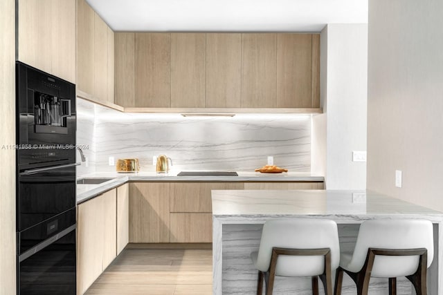 kitchen featuring light stone countertops, tasteful backsplash, light brown cabinets, and light hardwood / wood-style flooring