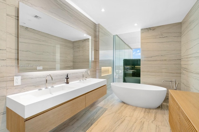 bathroom featuring tile walls, large vanity, double sink, and a bath to relax in