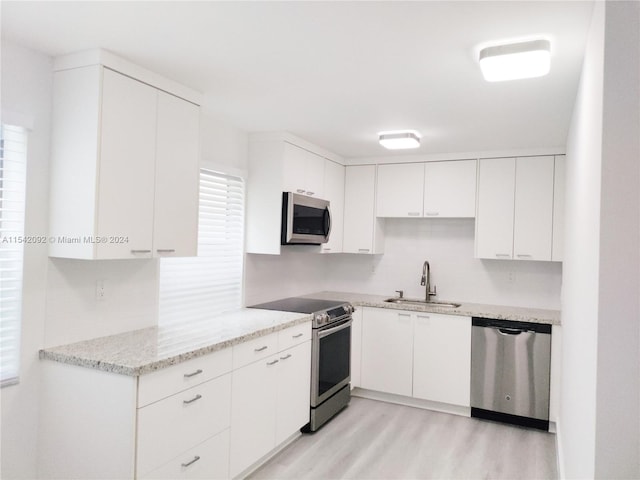 kitchen featuring light stone countertops, white cabinets, stainless steel appliances, sink, and light hardwood / wood-style flooring