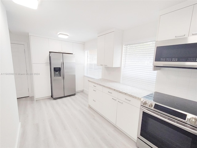 kitchen with white cabinets, light stone counters, stainless steel appliances, and light hardwood / wood-style flooring