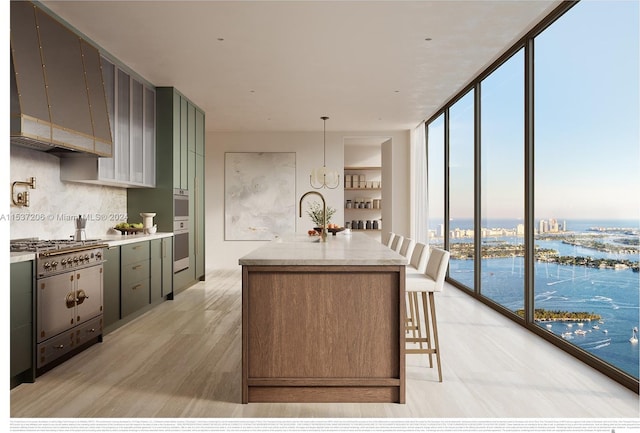 kitchen featuring floor to ceiling windows, a center island with sink, a water view, premium range hood, and tasteful backsplash