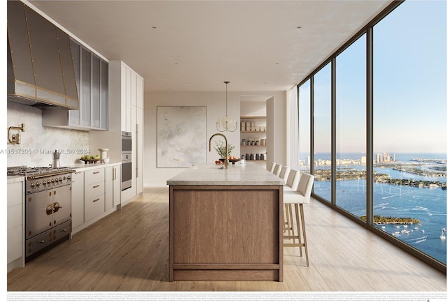 kitchen with light hardwood / wood-style floors, expansive windows, white cabinetry, a water view, and a kitchen island with sink