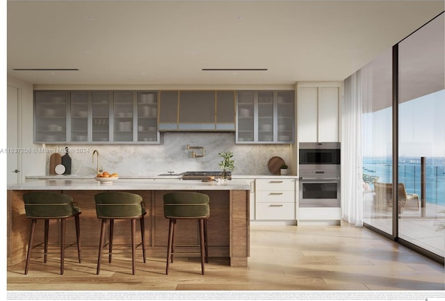 kitchen with backsplash, a kitchen bar, white cabinets, and light hardwood / wood-style flooring