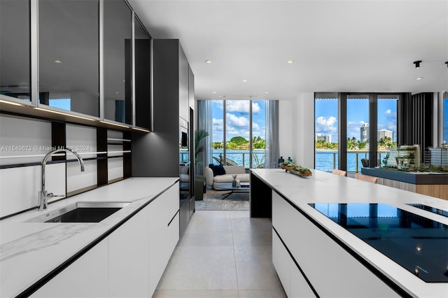 kitchen with white cabinets, a water view, light tile floors, and sink