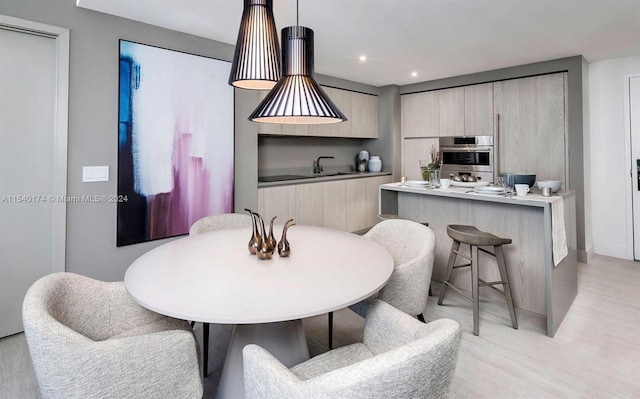 kitchen featuring pendant lighting, a kitchen breakfast bar, sink, light hardwood / wood-style flooring, and stainless steel double oven