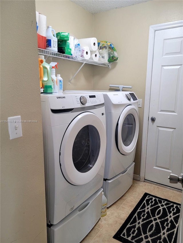 laundry room with light tile patterned floors, a textured ceiling, and washer and clothes dryer