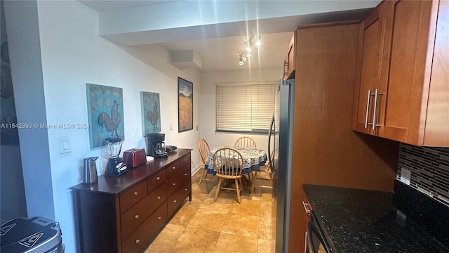 kitchen with pendant lighting, light tile floors, dark stone counters, backsplash, and stainless steel refrigerator