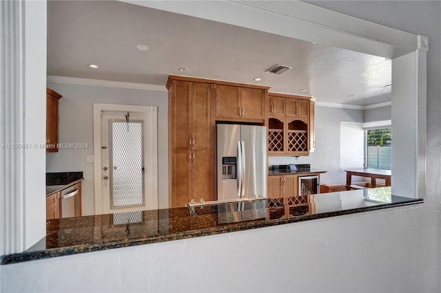 kitchen with kitchen peninsula, ornamental molding, appliances with stainless steel finishes, and dark stone counters