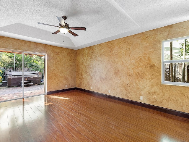 unfurnished room with a textured ceiling, ceiling fan, a wealth of natural light, and dark wood-type flooring