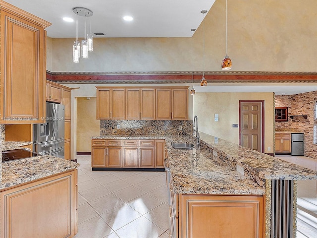 kitchen featuring pendant lighting, backsplash, sink, light stone counters, and stainless steel fridge