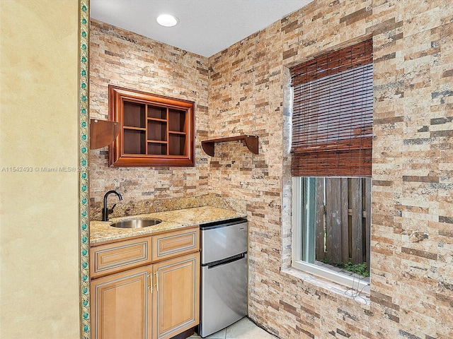 kitchen featuring light stone counters, sink, brick wall, and stainless steel fridge