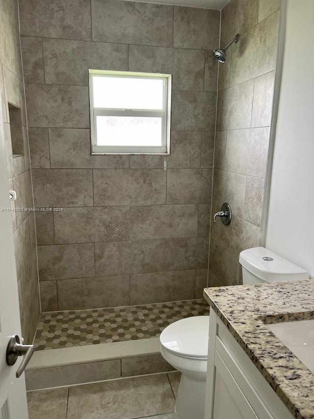 bathroom with a tile shower, tile flooring, vanity, and toilet