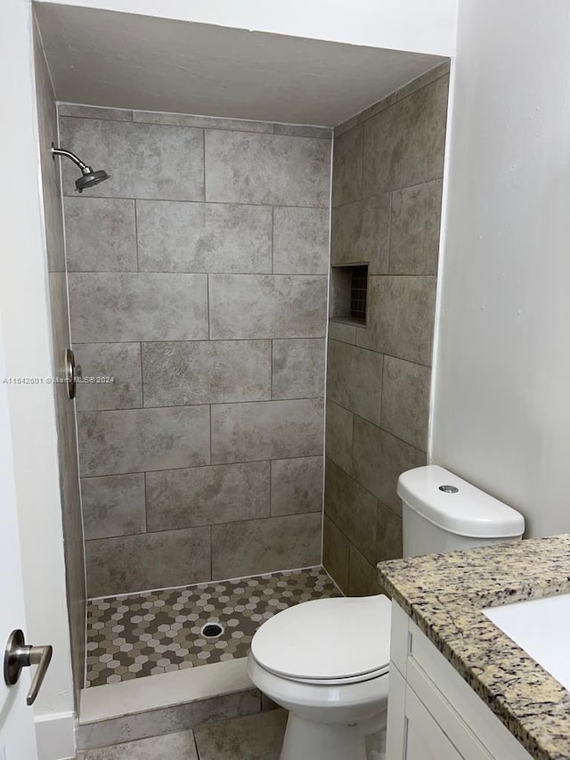 bathroom with tiled shower, vanity, toilet, and tile floors