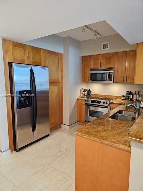 kitchen with stainless steel appliances, light stone counters, track lighting, light tile floors, and sink