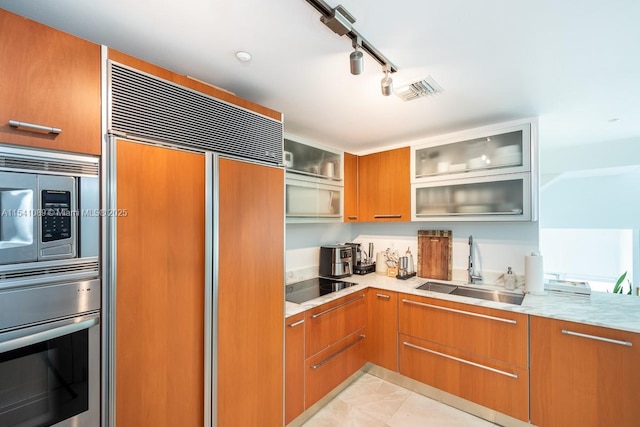 kitchen featuring track lighting, sink, built in appliances, light stone countertops, and light tile patterned flooring