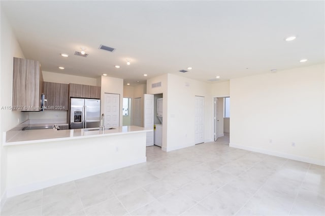 kitchen with sink, stacked washer and dryer, stainless steel fridge, and light tile flooring