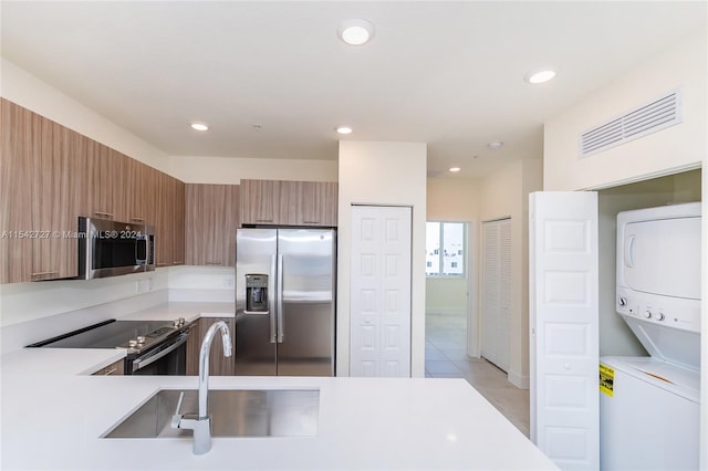 kitchen with light tile floors, appliances with stainless steel finishes, stacked washing maching and dryer, and sink