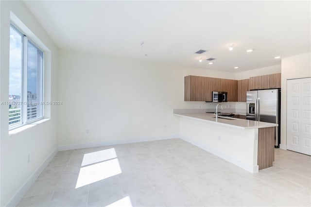 kitchen with light tile flooring, kitchen peninsula, appliances with stainless steel finishes, and sink