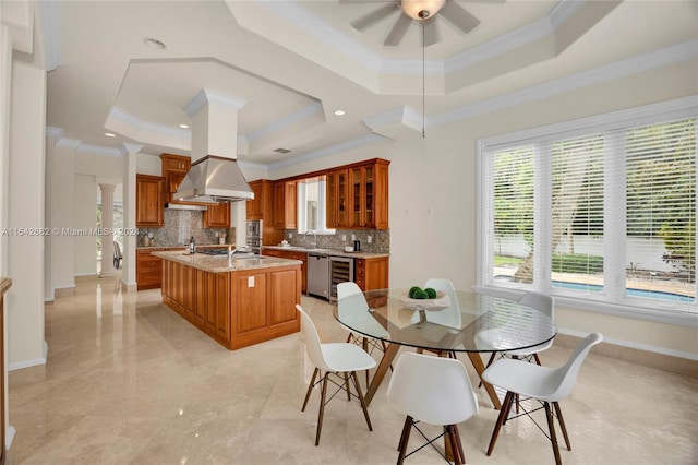 dining space with sink, beverage cooler, ceiling fan, a raised ceiling, and crown molding