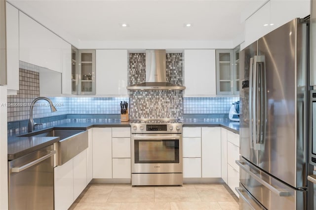 kitchen with white cabinetry, backsplash, stainless steel appliances, light tile floors, and wall chimney range hood