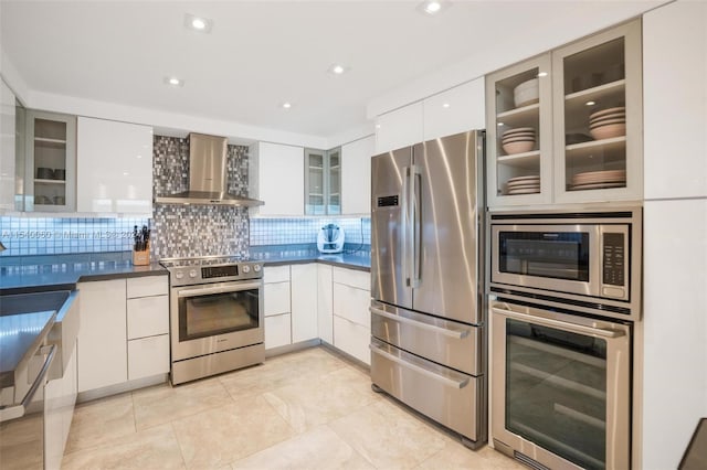 kitchen with backsplash, appliances with stainless steel finishes, light tile floors, white cabinets, and wall chimney exhaust hood