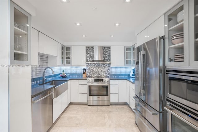 kitchen featuring stainless steel appliances, light tile floors, tasteful backsplash, wall chimney exhaust hood, and white cabinets