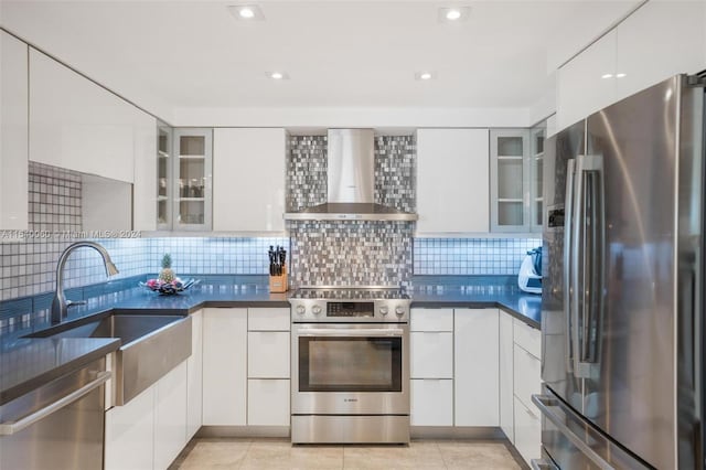 kitchen with light tile floors, white cabinets, backsplash, stainless steel appliances, and wall chimney exhaust hood