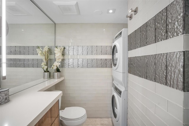 bathroom featuring tile walls, toilet, stacked washer / dryer, and vanity