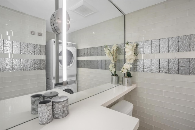 bathroom featuring tile walls, stacked washer / dryer, and toilet