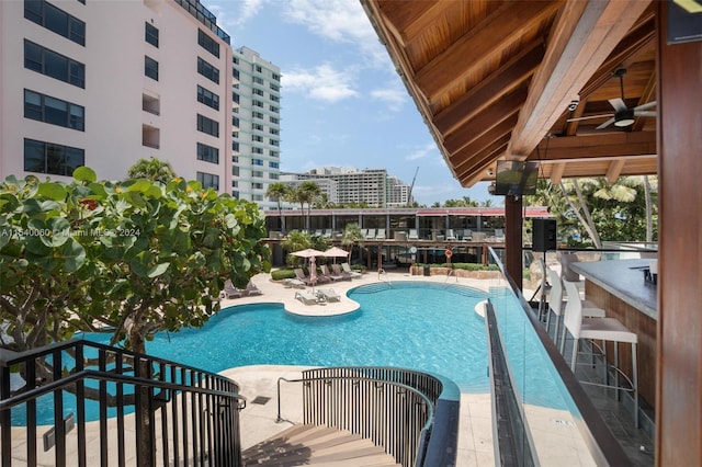 view of swimming pool featuring a bar, ceiling fan, and a patio