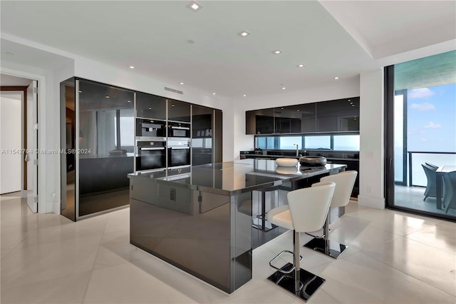 kitchen featuring sink, double oven, light tile flooring, a kitchen bar, and a center island