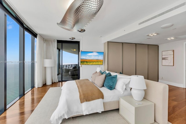 bedroom featuring visible vents, wood finished floors, floor to ceiling windows, baseboards, and access to exterior