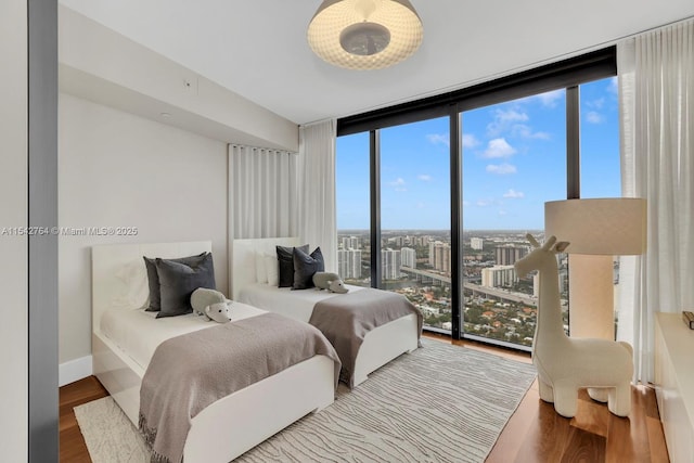 bedroom featuring expansive windows, baseboards, wood finished floors, and a view of city