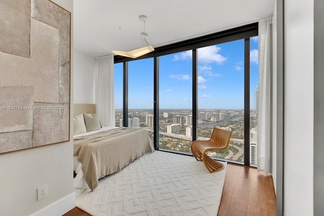 bedroom featuring a city view, a wall of windows, baseboards, and wood finished floors