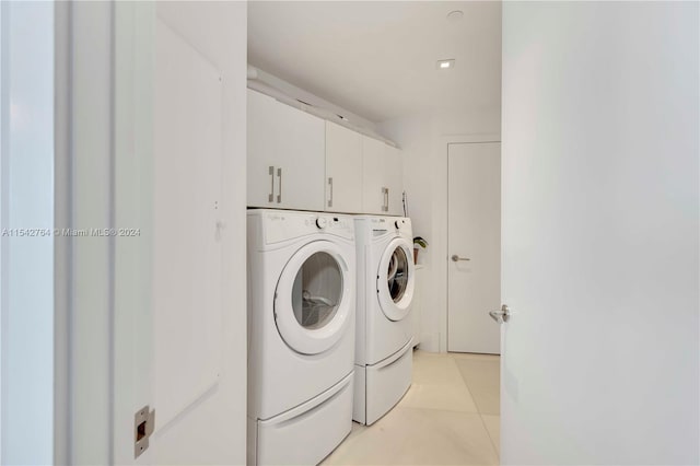 clothes washing area featuring light tile floors, washing machine and dryer, and cabinets