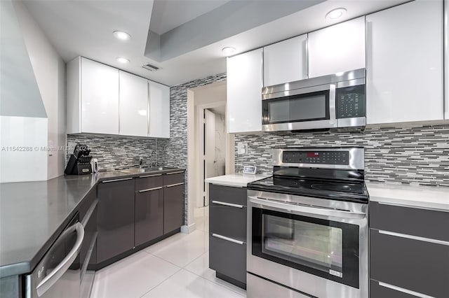 kitchen with sink, decorative backsplash, light tile patterned floors, appliances with stainless steel finishes, and white cabinetry