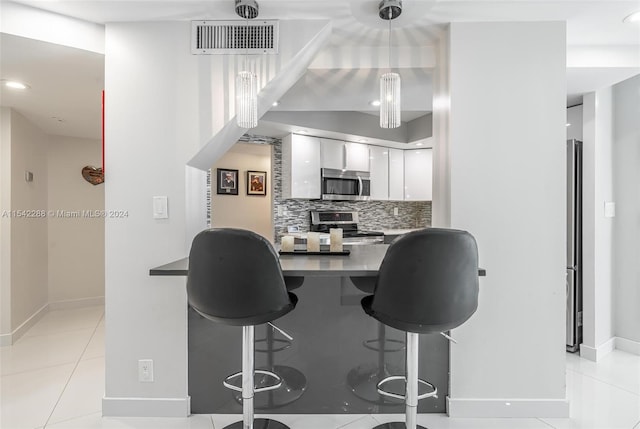 kitchen featuring stainless steel appliances, light tile patterned floors, decorative backsplash, a breakfast bar, and white cabinets