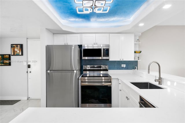 kitchen featuring decorative backsplash, appliances with stainless steel finishes, a tray ceiling, sink, and white cabinets