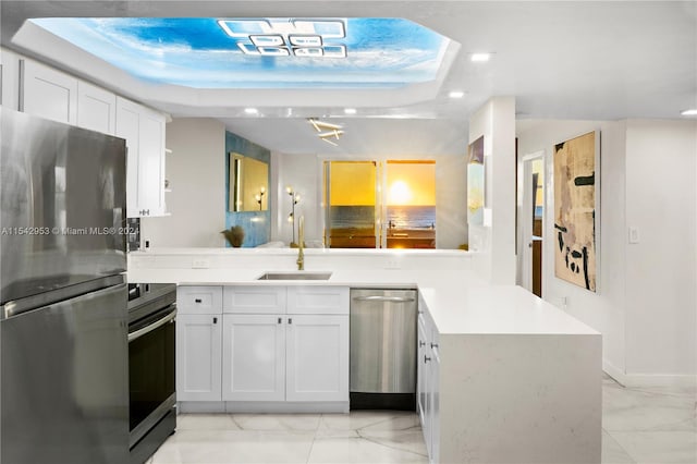 kitchen with a raised ceiling, kitchen peninsula, white cabinets, and stainless steel appliances