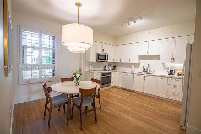 kitchen with stainless steel appliances, decorative light fixtures, light hardwood / wood-style flooring, white cabinets, and sink